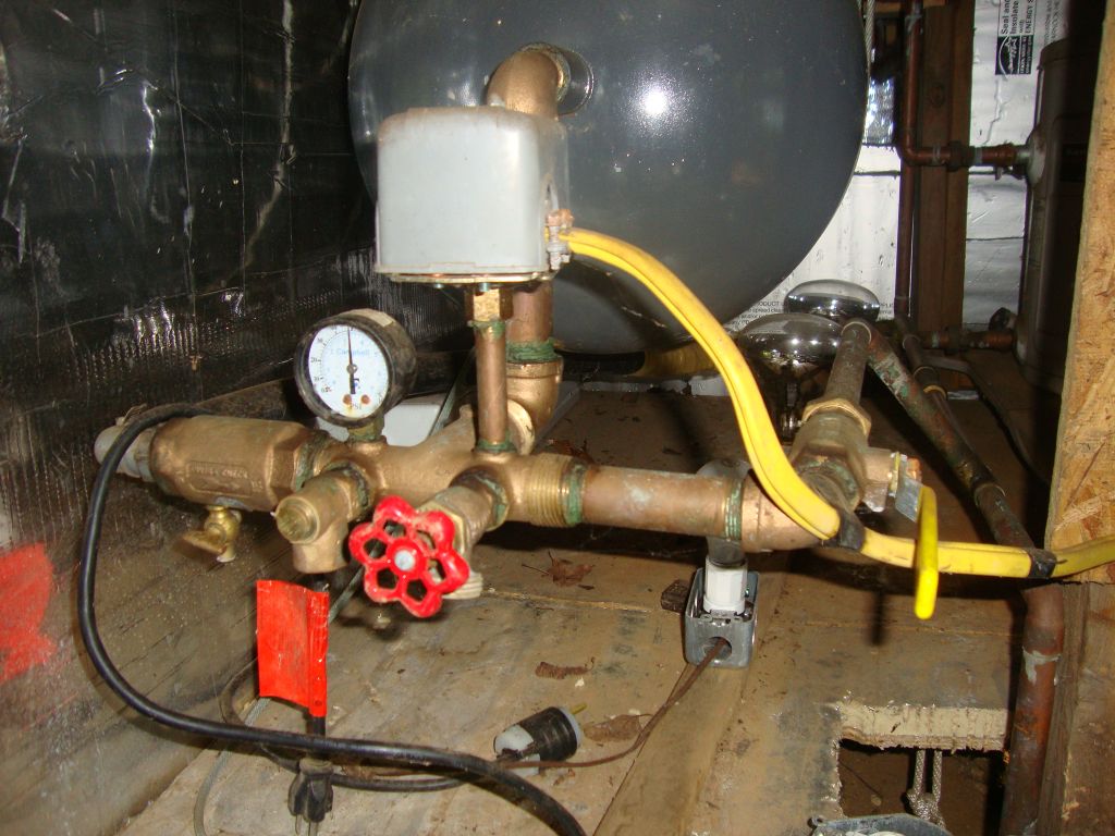 Plumbing at the lake end
The little air bleeder valve at the left, now closed for system use, is hard to open (vertical) without pliers. I use a garden hose on the red faucet as the main drain for the system, but draining must be finished with the lake valve down below in the cathouse. The horizontal yellow-handled valve opens and closes water to the cabin. I learned about this one once when all seemed fine but I had no water inside. For some reason, I had closed this valve (vertical); opening it (like this) gave the cabin its water.  